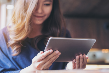 A beautiful Asian woman with smiley face holding and using tablet pc in modern cafe