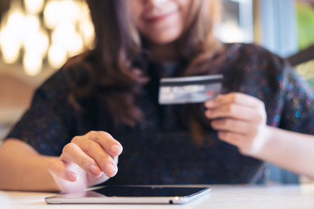 A smiley face Asian woman holding credit card and using tablet pc in restaurant with feeling happyの写真素材