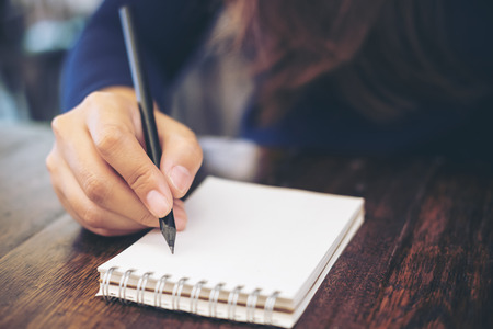 Close up image of woman's hand writing on notebook with wooden table backgroundの写真素材