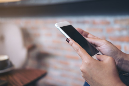 Closeup image of a woman's hands holding mobile phone with blur background in cafe
