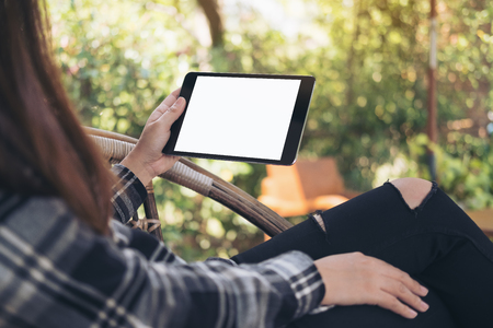 Mockup image of woman's hand holding black tablet pc with blank white screen while sitting outdoor with green nature backgroundの写真素材