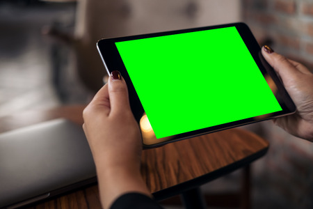 Mockup image of a woman holding black tablet pc with blank green desktop screen in cafeの写真素材
