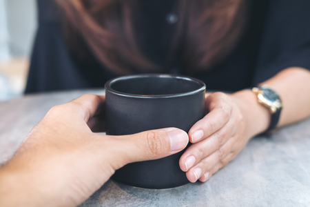 A man and a woman holding a black coffee cup together on the tableの写真素材