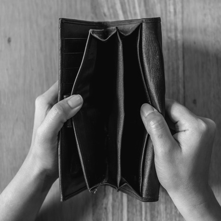 Top view black and white image of woman's hands open an empty black leather wallet with wooden table backgroundの写真素材