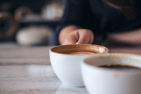Close up image of two people clink white coffee mugs on wooden table in cafeの写真素材