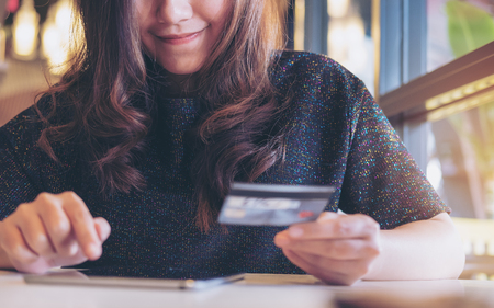 A smiley face Asian woman holding credit card and using tablet pc in restaurant with feeling happyの写真素材