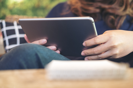 A woman holding , using and pointing at tablet pc sitting in modern cafe with green nature...