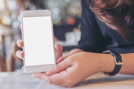 Mockup image of a woman holding and showing white mobile phone with blank screen on the table in modern cafe Mockup image of a woman holding and showing white mobile phone with blank screen on the table in modern cafe