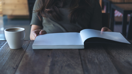 Closeup image of a woman reading a book with white coffee mug on wooden table in vintage cafeの写真素材