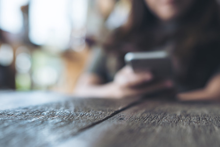 Blur image of a woman holding and using smart phone on wooden table in vintage cafeの写真素材