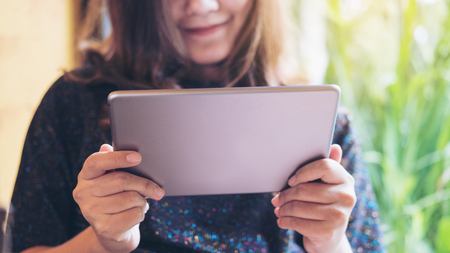 A beautiful Asian woman with smiley face holding , using and looking at tablet pc in modern cafe with green nature backgroundの写真素材