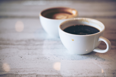 Closeup image of two white cups of hot latte coffee and Americano coffee on marble table in modern cafeの写真素材