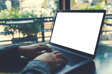Mockup image of business woman using and typing on laptop with blank white screen on table in modern cafeの写真素材