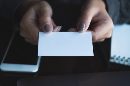 Business woman holding and giving  business card to someone with mobile phone and notebook on table in officeの写真素材