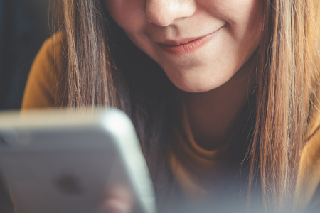 Closeup image of a beautiful Asian woman holding , using and looking at smart phone in cafeの写真素材