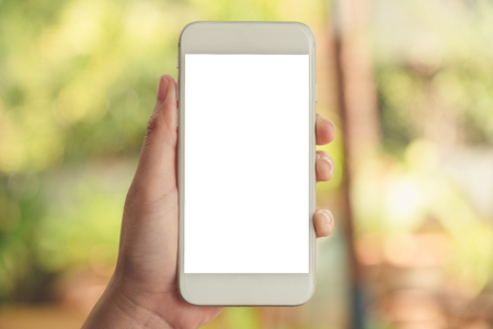 Mockup image of a hand holding and showing white smart phone with blank desktop screen in outdoor with blur green nature backgroundの写真素材