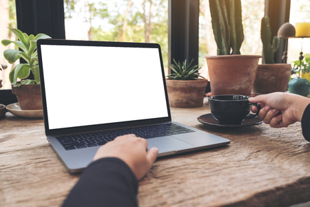 Mockup image of woman using and typing on laptop with blank white desktop screen on vintage wooden table in cafeの写真素材