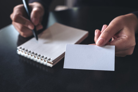 Businesswoman giving and showing an empty business card while writing down on a notebookの写真素材