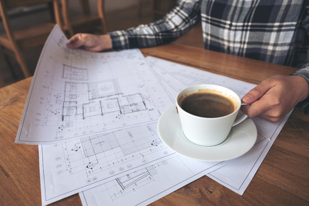 An architect working on shop drawing paper while drinking coffee in officeの写真素材