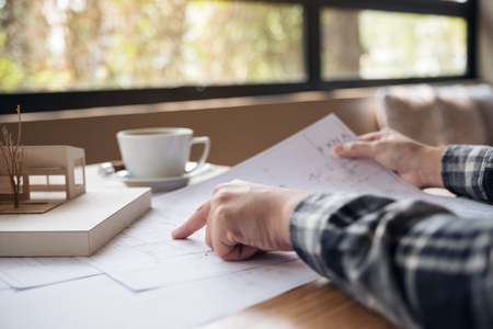 An architect working on an architecture model with shop drawing paper and coffee cup on tableの写真素材