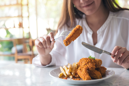 Closeup image of a beautiful asian woman enjoy eating french fries and fried chicken in restaurantの写真素材