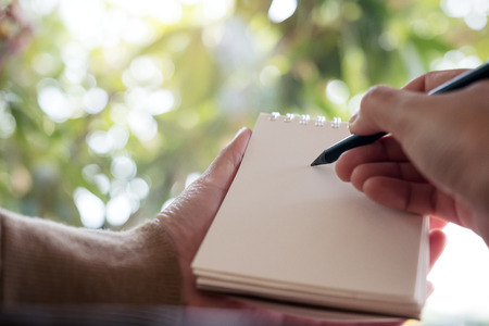Closeup image of hands holding and writing down on a blank notebook with blur nature backgroundの写真素材