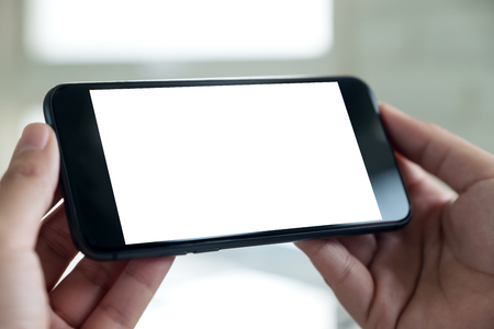 Mockup image of a hand holding black
mobile phone with blank white desktop screen の写真素材
