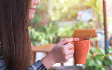 Closeup image of an Asian woman holding and drinking hot coffee with feeling good in the gardenの写真素材