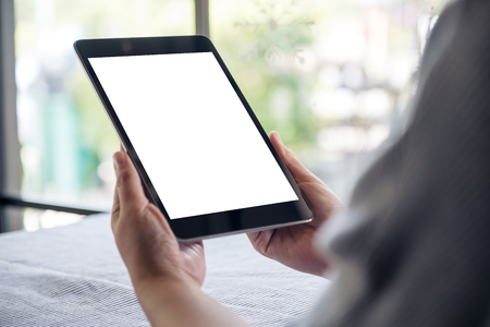 Mockup image of hands holding black tablet pc with blank white desktop screen on table with blur background in cafe の写真素材