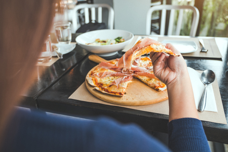 Closeup image of a woman picking a piece of Parma ham pizza up to eat in the restaurantの写真素材