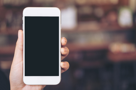 Mockup image of a hand holding white mobile phone with blank black desktop screen with blur backgroundの写真素材