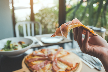 Closeup image of a hand picking a piece of Parma ham pizza up to eat in the restaurantの写真素材