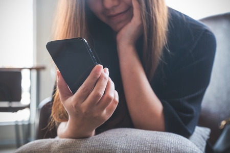 Closeup image of a beautiful Asian woman holding , using and looking at smart phone with feeling happyの写真素材