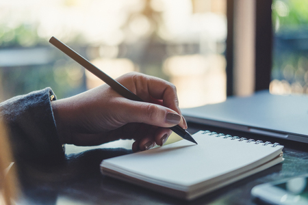 Closeup image of a woman's hands writing on notebook on the table の写真素材