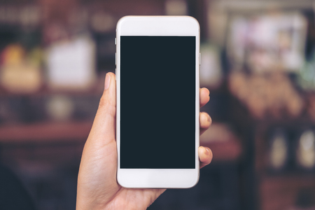 Mockup image of a hand holding white mobile phone with blank black desktop screen with blur backgroundの写真素材