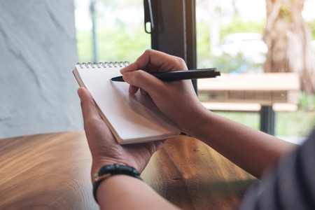 Closeup image of a woman's hands writing down on a white blank notebook 
