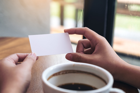 Hands holding an empty business card with coffee cup on tableの写真素材