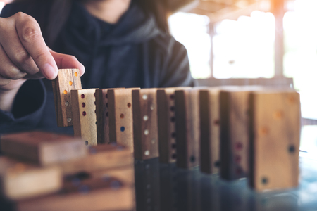 Closeup image of a woman putting wooden domino game in order on tableの写真素材