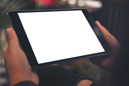 Top view mockup image of a woman sitting cross legged and holding black tablet pc with blank white desktop screen in cafeの写真素材