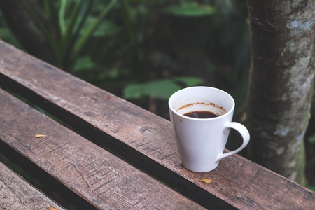 Closeup image of a cup of hot coffee on wooden bench in green nature backgroundの写真素材