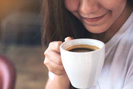 Closeup image of an Asian woman holding a coffee cup before drinking with feeling good in cafeの写真素材