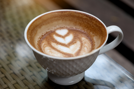Closeup image of a cup of hot latte coffee with heart latte art on tableの写真素材