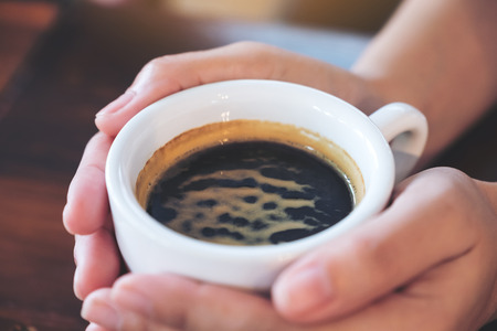 Closeup image of hands holding a cup of hot coffee on wooden table in cafeの写真素材