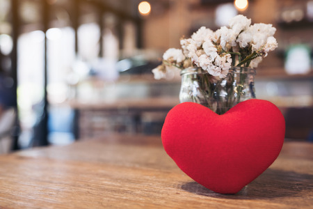 A red heart sign with flower vase on wooden table in cafeの写真素材