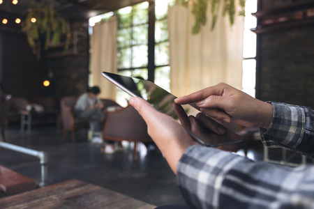 Closeup image of hands holding and using tablet pc in modern cafe