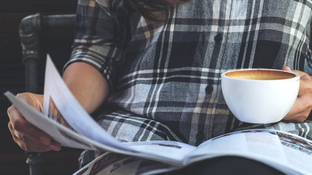 Closeup image of a woman reading a book while drinking coffee in modern cafe の写真素材