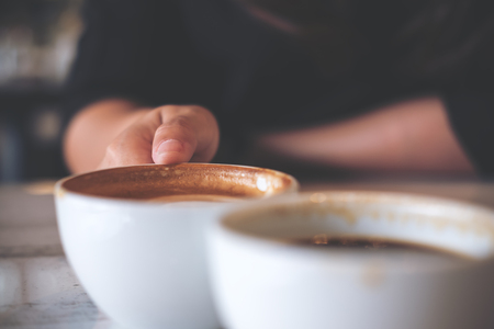 Close up image of two people clink white coffee mugs on wooden table in cafeの写真素材