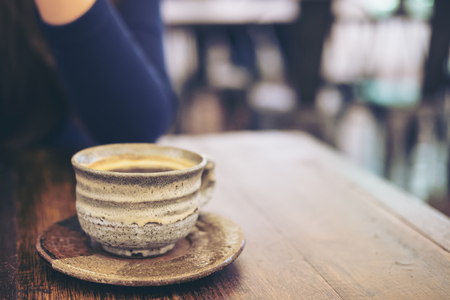 Closeup image of a woman sitting in cafe with ceramics cup of hot coffee on vintage wooden table in cafeの写真素材