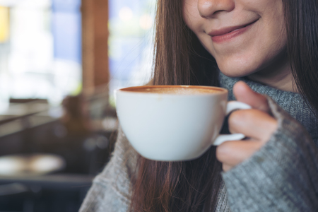Closeup image of an Asian woman holding and drinking hot coffee in winter timeの写真素材