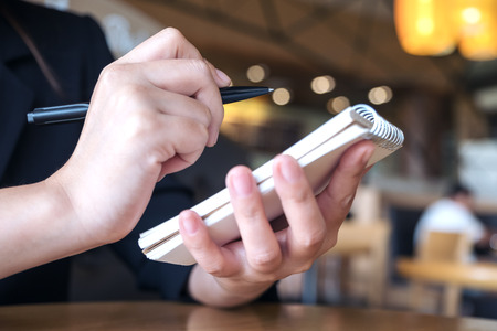 Closeup image of a hand holding and writing down on a notebook on table 